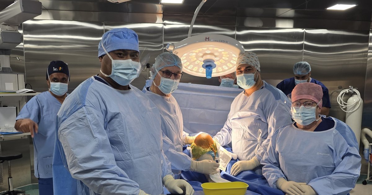 Members of the surgical team in gowns, masks and caps around an operating table; the patient is covered by surgical drapes