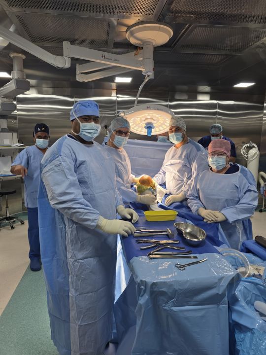 Members of the surgical team in gowns, masks and caps around an operating table, with instruments on a draped tray in the foreground; the patient is covered by surgical drapes. Left to right: Dr Tangi, Poasi, Dr van Dalen, Dr Tevita Tu'ungafasi and Lynette Sweetman