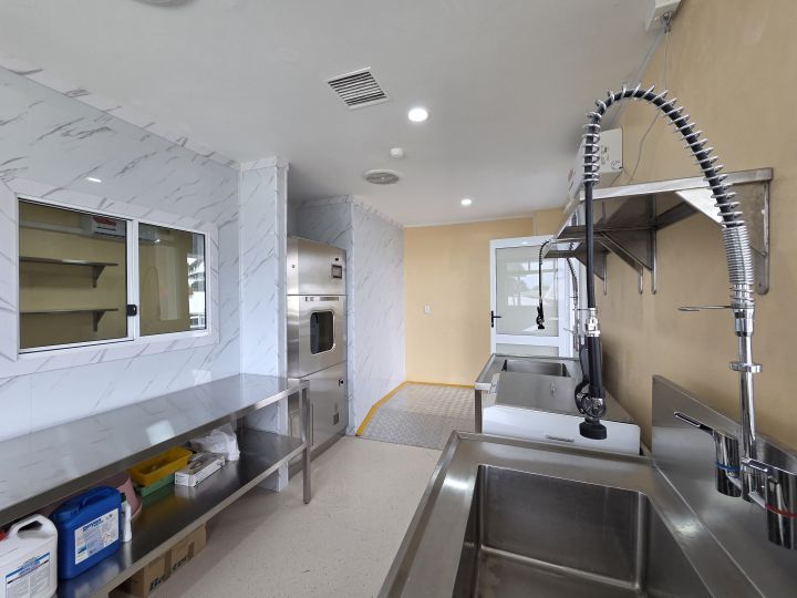 A clean stainless-steel sterilisation room with a large sink and pre-rinse tap, a wall-mounted steriliser, and a long worktable